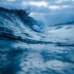 Ocean wave curling against cloudy sky